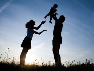Silhouette of parents raising infant towards the sky.